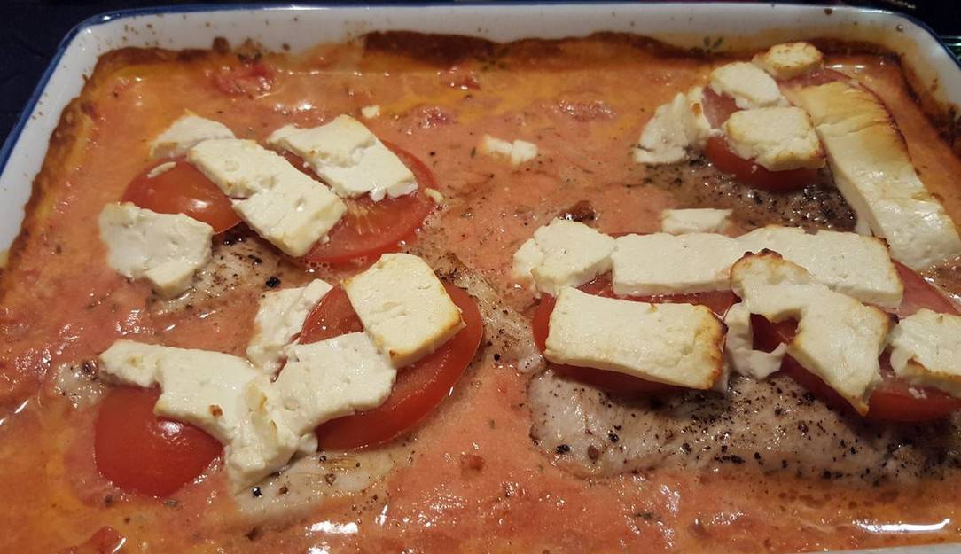 Putenschnitzel mit Tomatenscheiben und Schafskäse belegen
